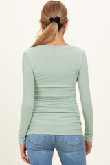 woman wearing a light green long sleeve maternity top with a fitted silhouette and gathered detailing at the sides
