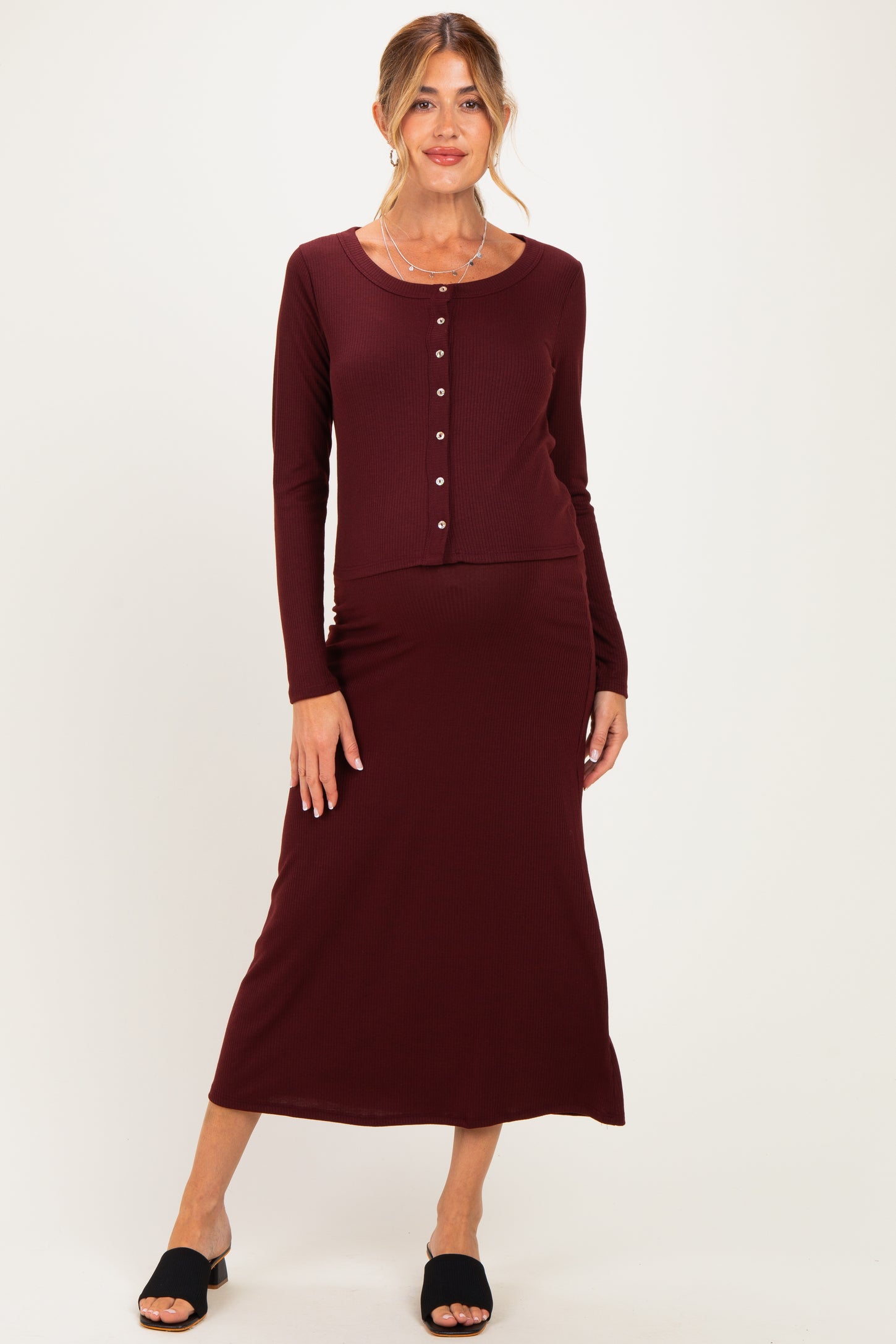 woman wearing a burgundy long sleeve maternity dress with a button-up top and a fitted maxi skirt, showing a baby bump