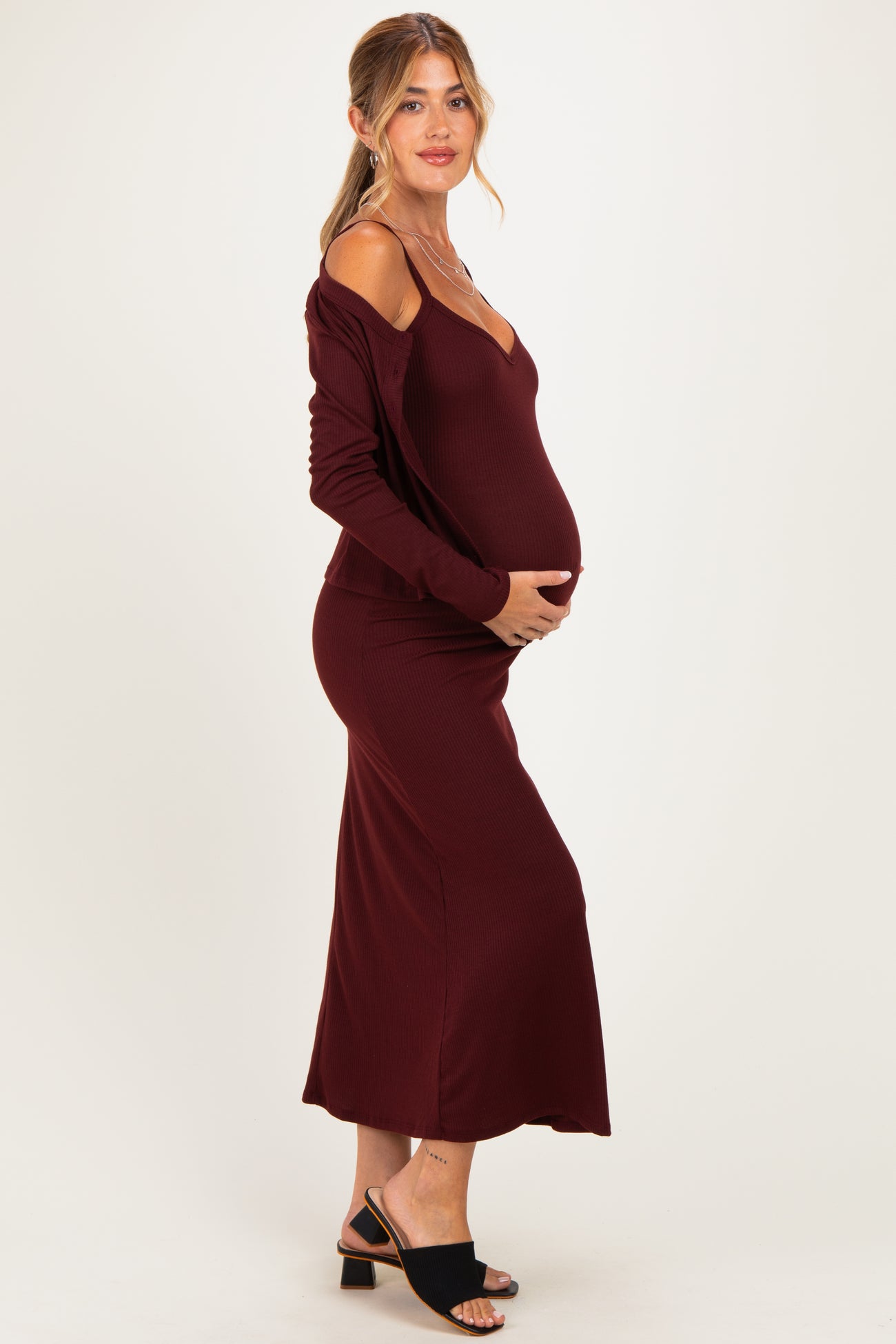 woman wearing a burgundy off-shoulder maternity dress, highlighting her baby bump and styled with black sandals