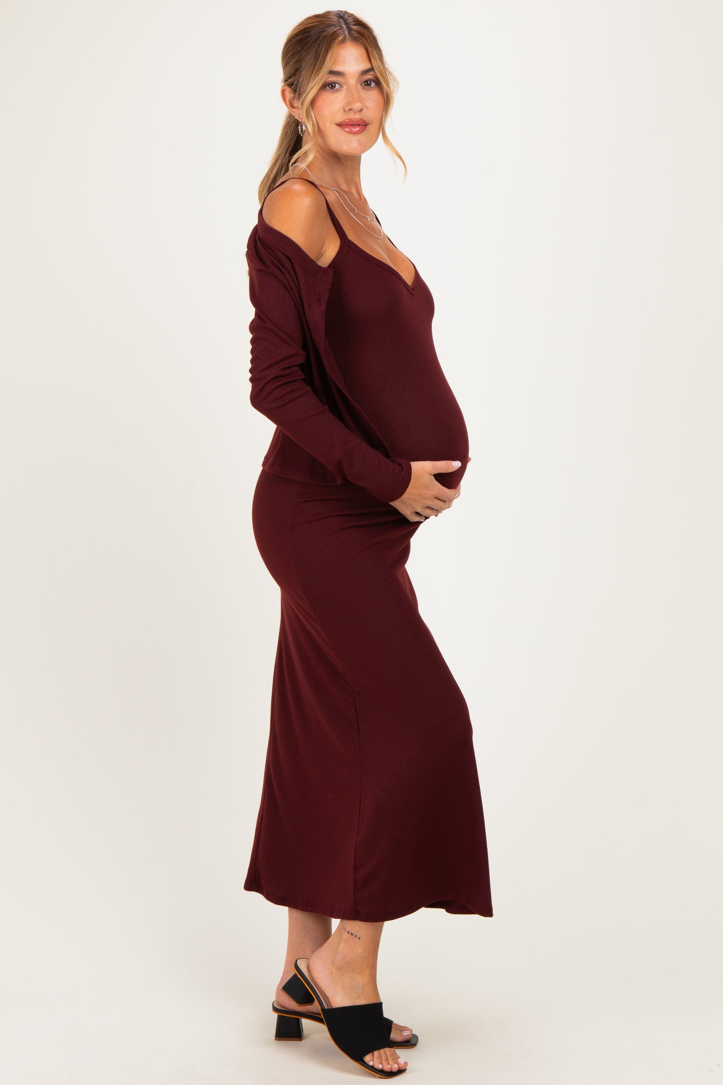 woman wearing a burgundy off-shoulder maternity dress, highlighting her baby bump and styled with black sandals