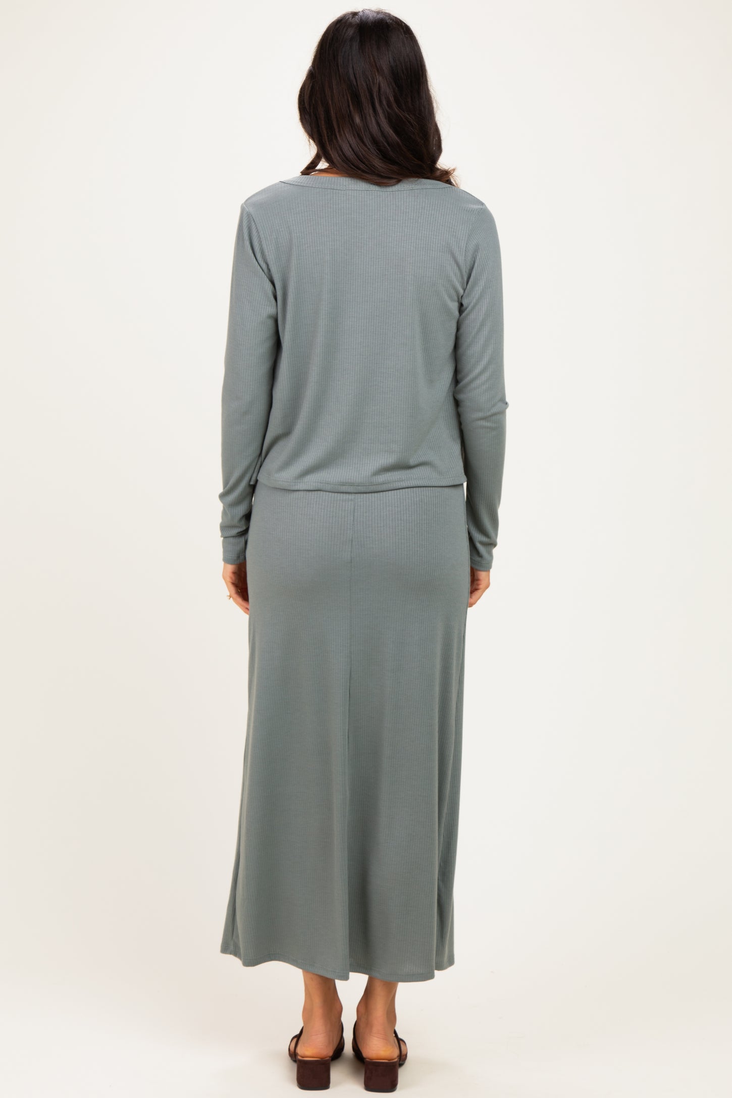 woman wearing a long sleeve light green maxi dress, viewed from the back, with a fitted waist and a flowy skirt