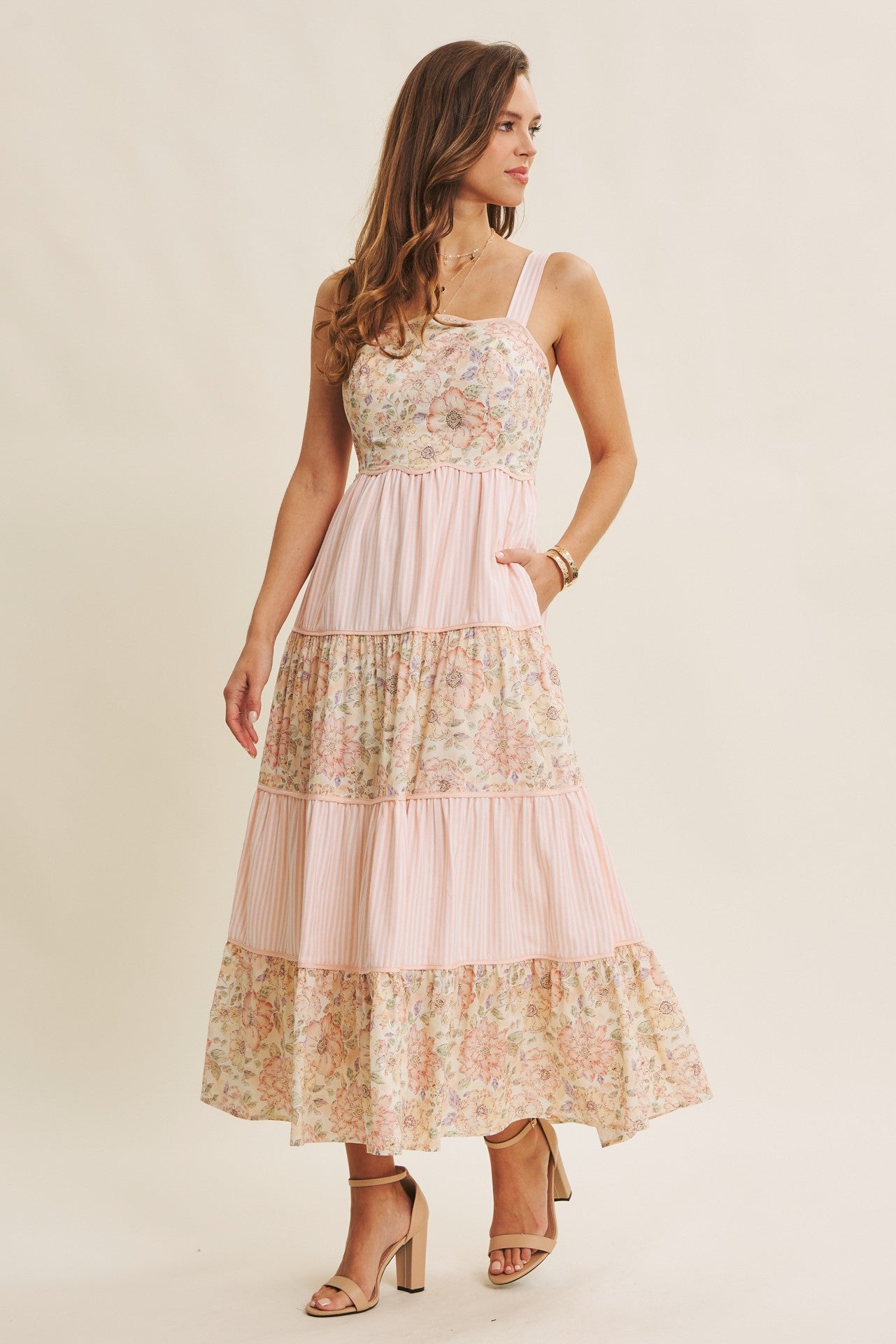woman wearing a floral tiered maxi dress with pink stripes and a fitted bodice, standing elegantly