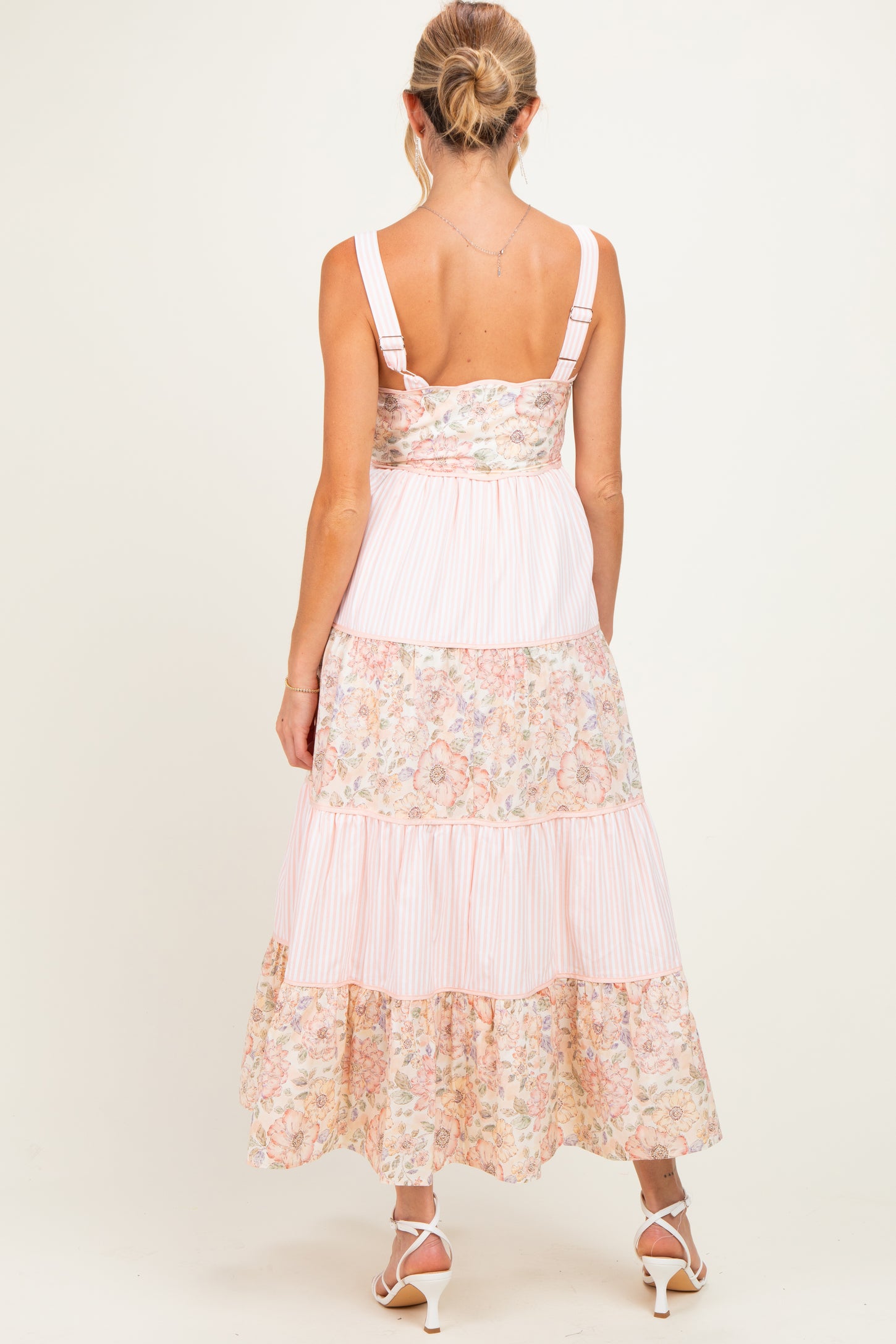 woman wearing a back view of a floral patterned maternity maxi dress with tiered ruffles and adjustable straps