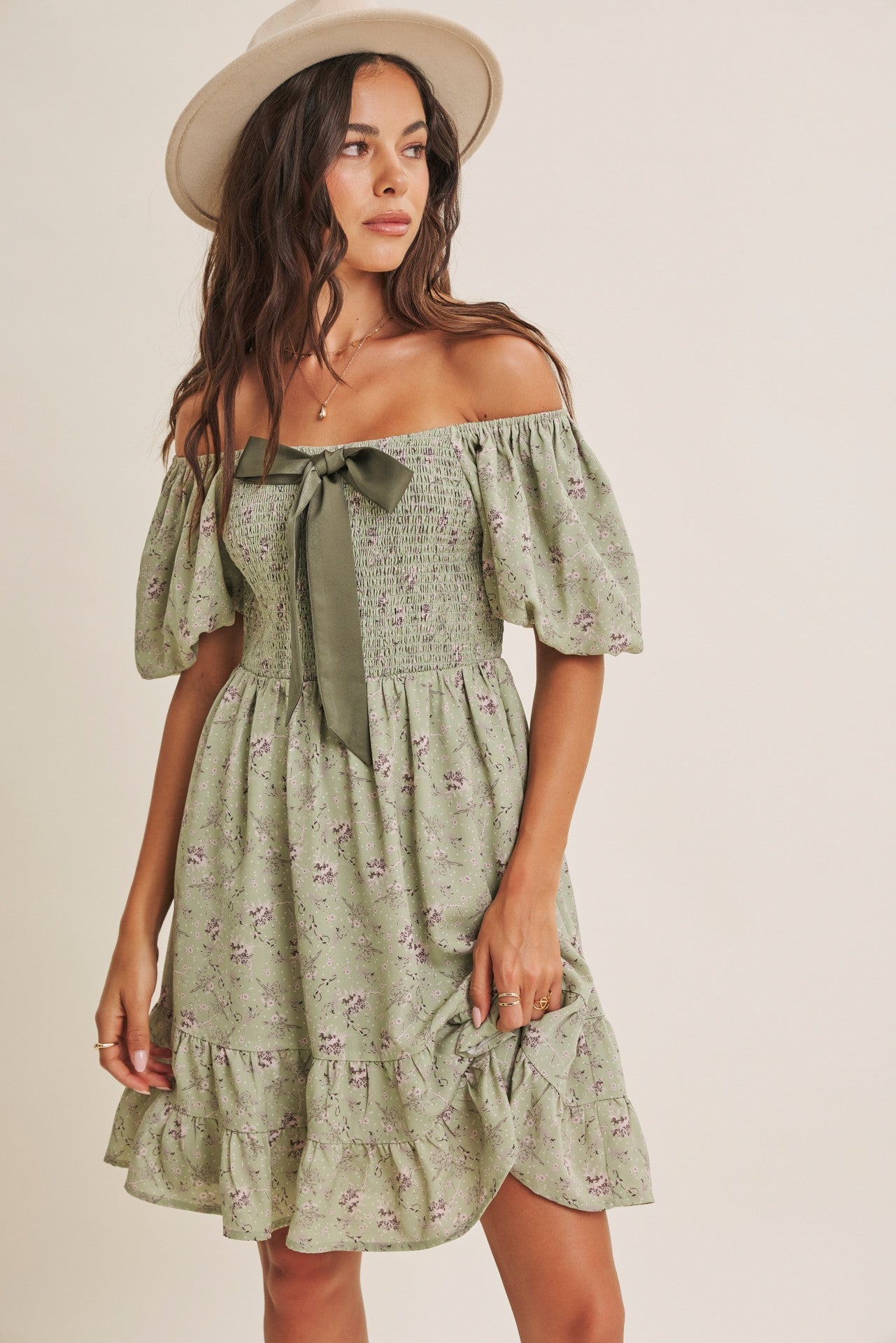 woman wearing a green off-the-shoulder floral dress with puff sleeves and a ribbon tie detail