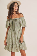 woman wearing a green off-the-shoulder floral dress with puff sleeves and a ribbon tie detail