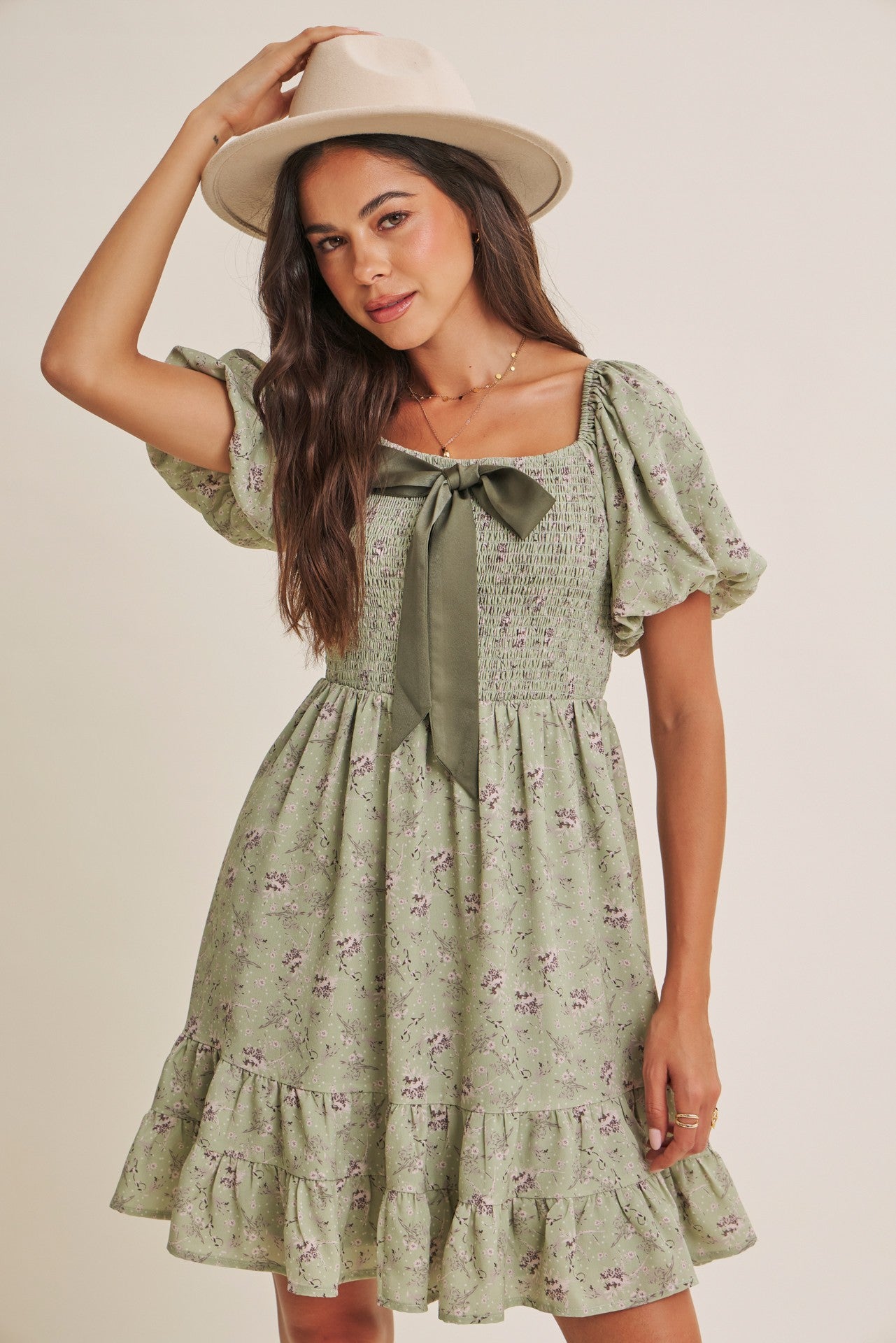 woman wearing a green floral smocked dress with puff sleeves and a bow detail, accessorized with a wide-brimmed hat