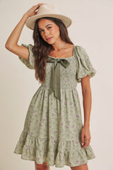 woman wearing a green floral smocked dress with puff sleeves and a bow detail, accessorized with a wide-brimmed hat