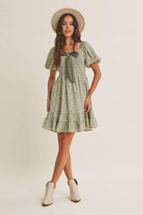 woman wearing a green floral puff sleeve dress with a bow detail and ruffled hem, paired with a beige hat and ankle boots