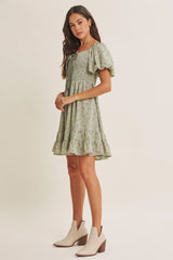 woman wearing a light green floral print short dress with puff sleeves and a ruffled hem