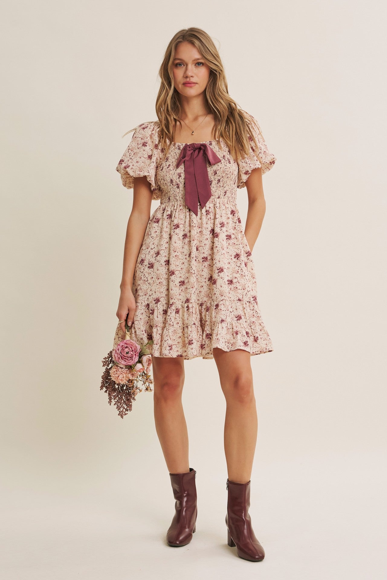 woman wearing a floral print dress with puff sleeves and a bow detail, holding a bouquet of flowers