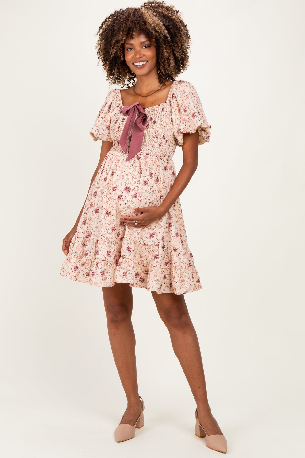 woman wearing a floral maternity dress with puff sleeves and a bow detail, holding her baby bump