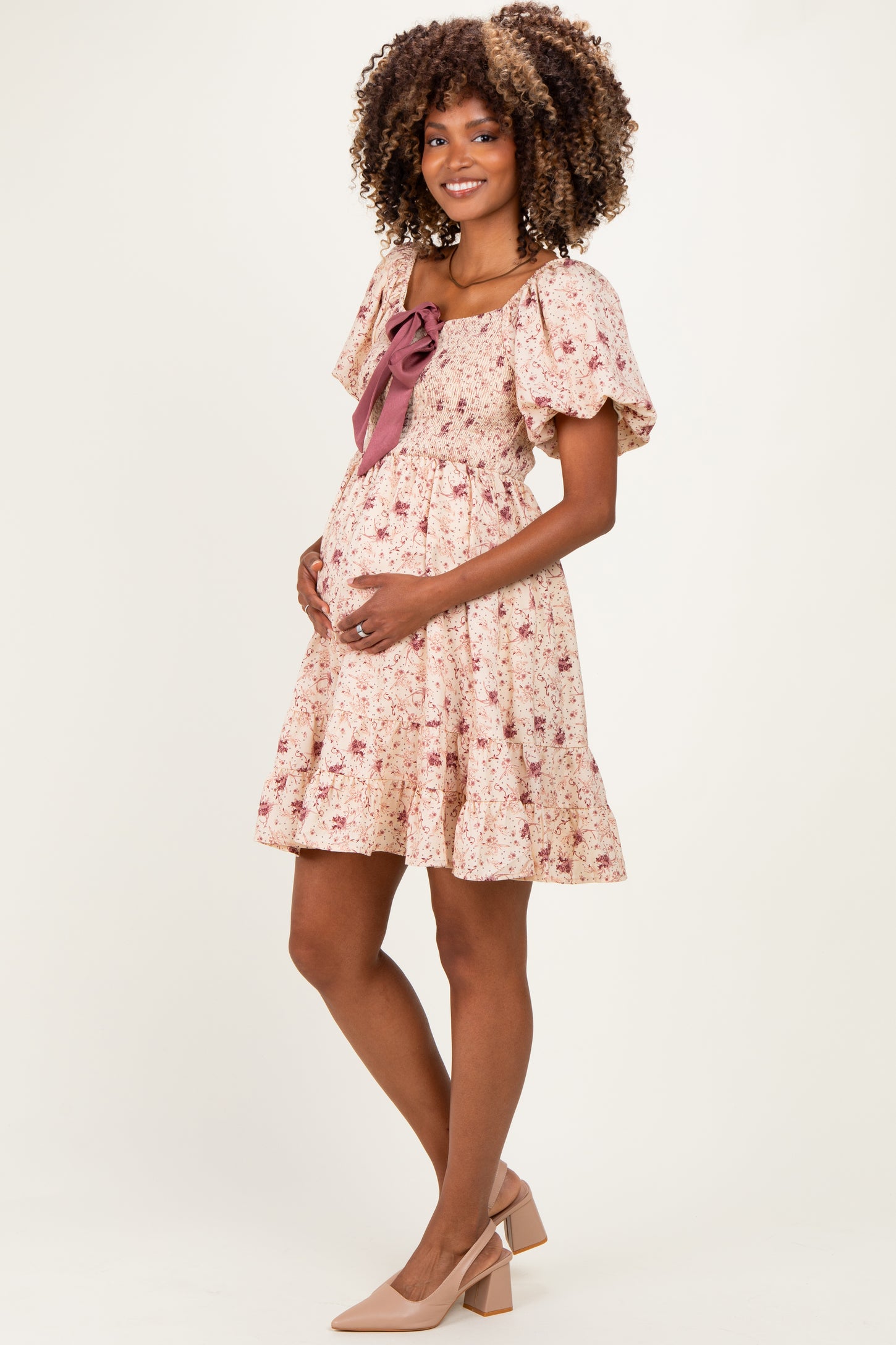woman wearing a floral printed maternity dress with puff sleeves and a bow detail, holding her baby bump