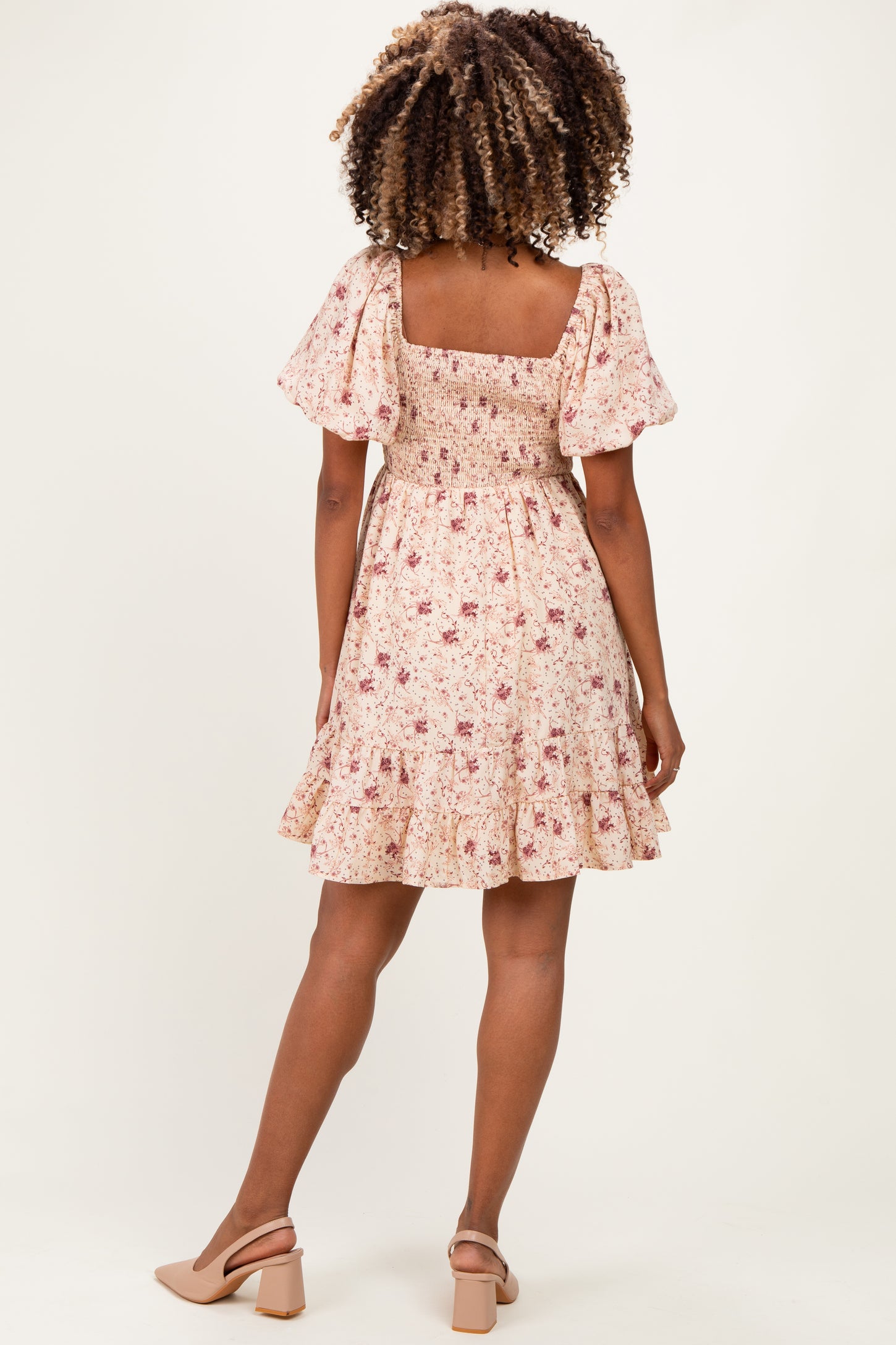 woman wearing a floral maternity dress with puff sleeves and a tiered skirt, showing her back