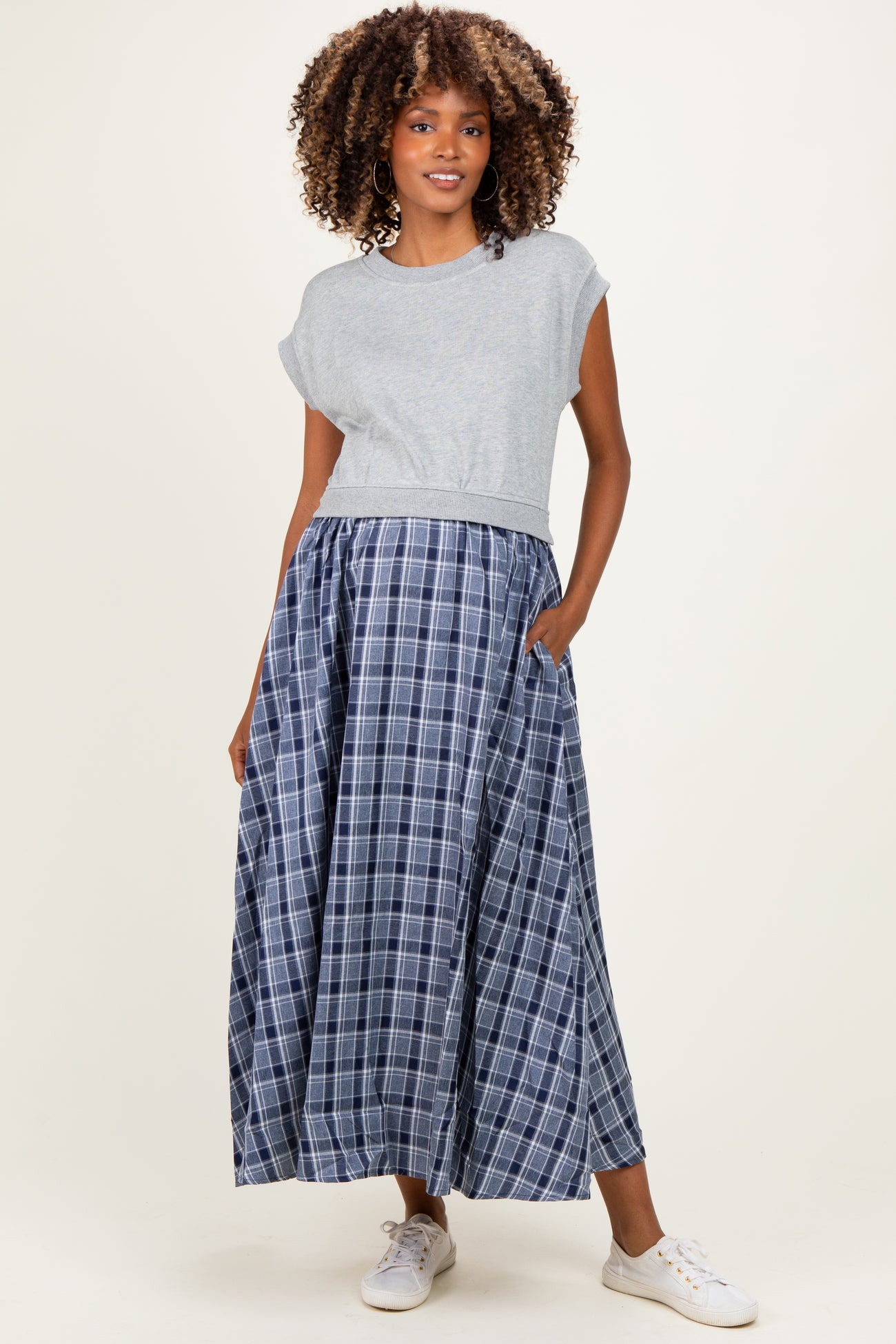 woman wearing a gray cropped maternity top and a long blue plaid maternity skirt with pockets