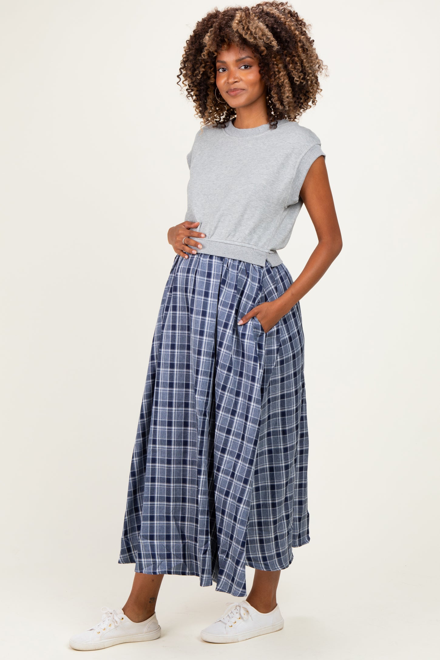 woman wearing a gray short sleeve top and a blue plaid maternity maxi skirt, showing her baby bump