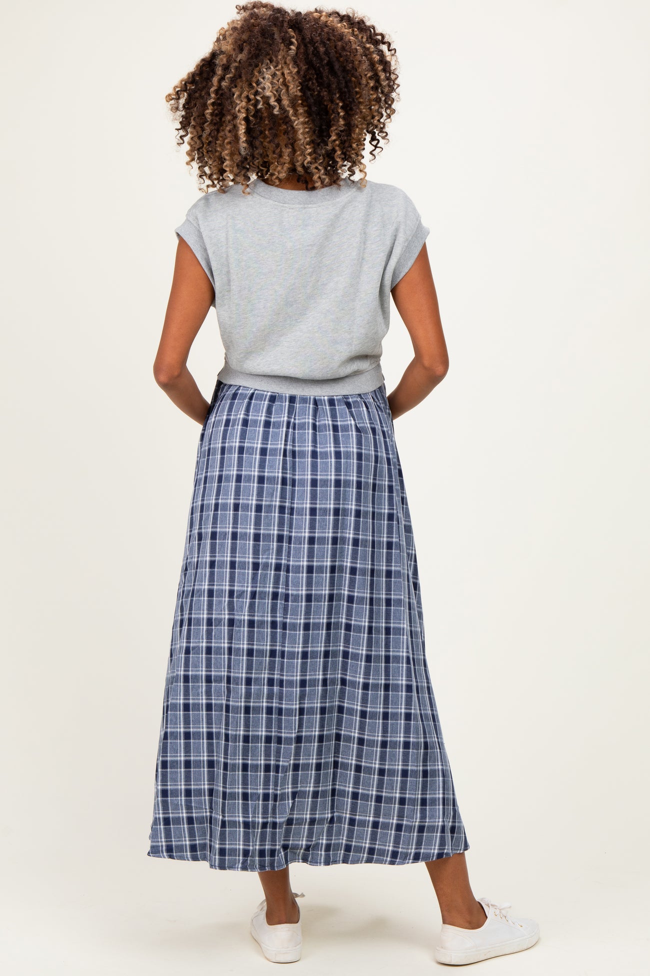 woman wearing a grey short sleeve top and a blue plaid maternity maxi skirt, showing a baby bump from the back