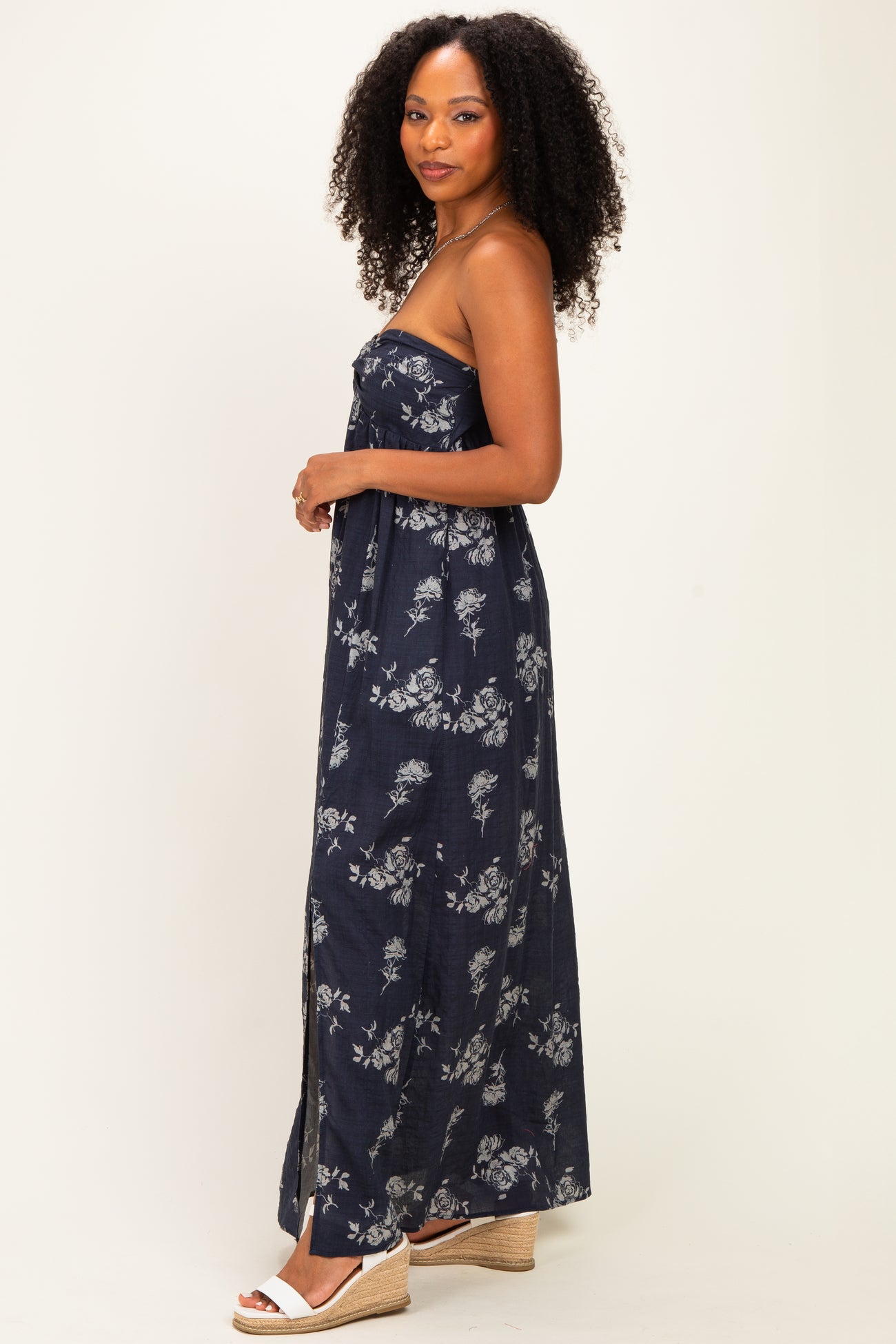 woman wearing a navy blue strapless maxi dress with white floral print and posing sideways