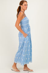 woman wearing a light blue sundress with white floral patterns and pockets, styled with thin straps and a scalloped hem