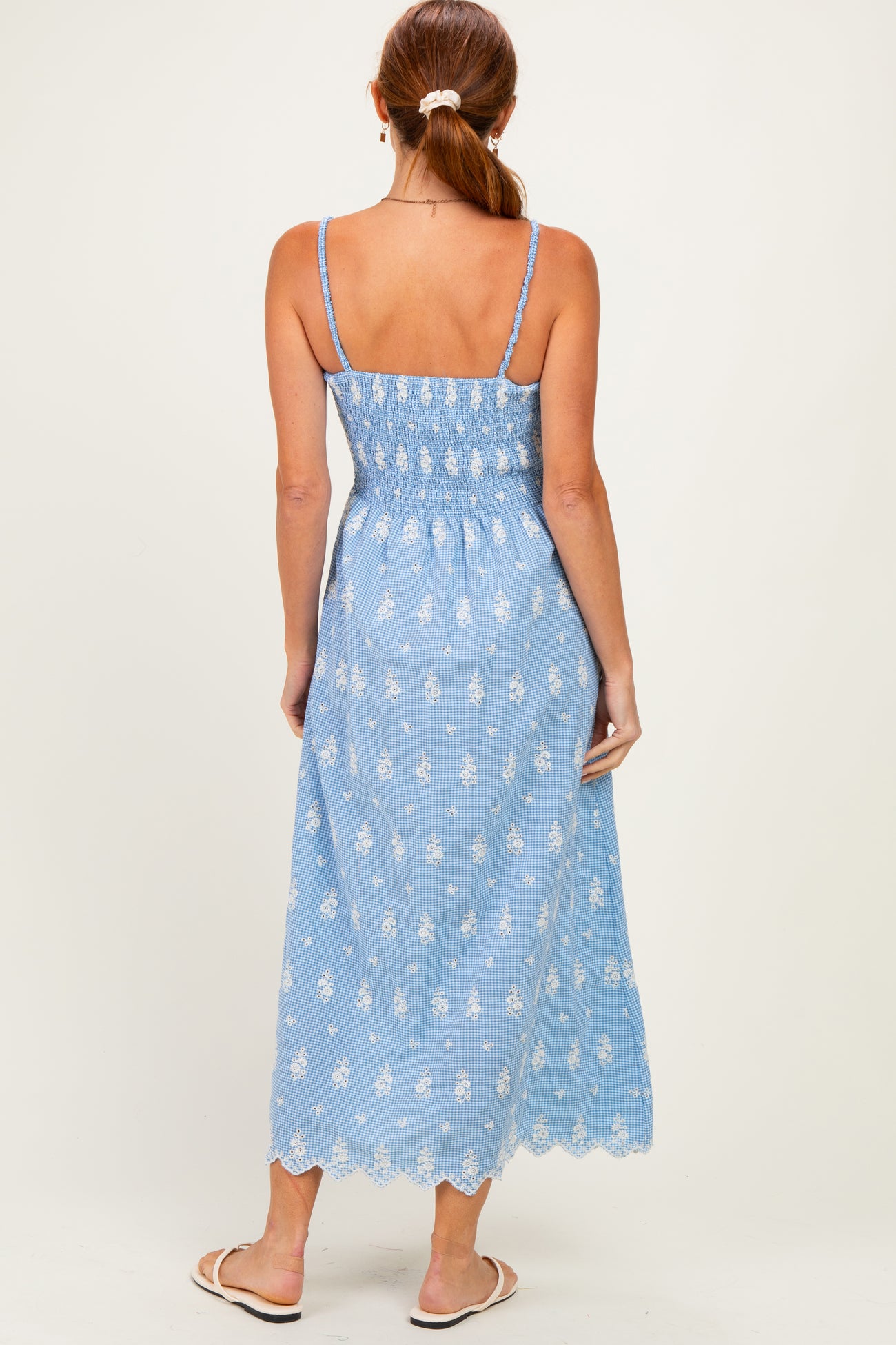 woman wearing a light blue maxi dress with a smocked bodice and white floral embroidery, viewed from the back