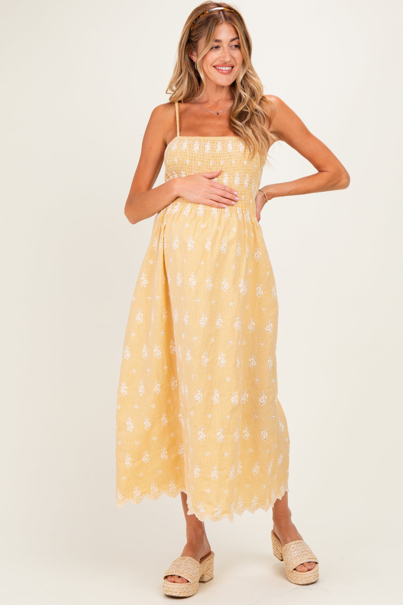 woman wearing a yellow maternity dress with white floral design and a fitted bodice, gently cradling her baby bump