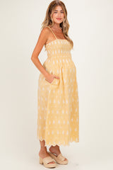 woman wearing a yellow smocked maternity dress with white floral patterns and pockets, showing her baby bump