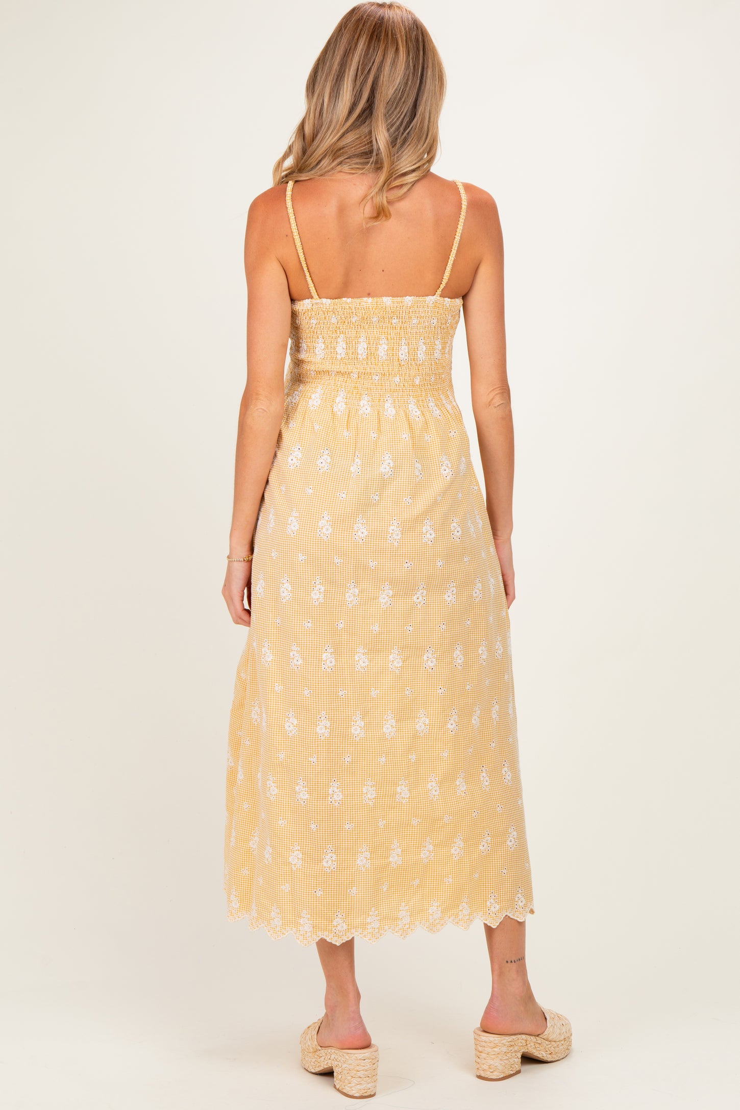 woman wearing a yellow maternity maxi dress with floral embroidery and adjustable straps, showing the back view