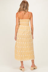 woman wearing a yellow maternity maxi dress with floral embroidery and adjustable straps, showing the back view