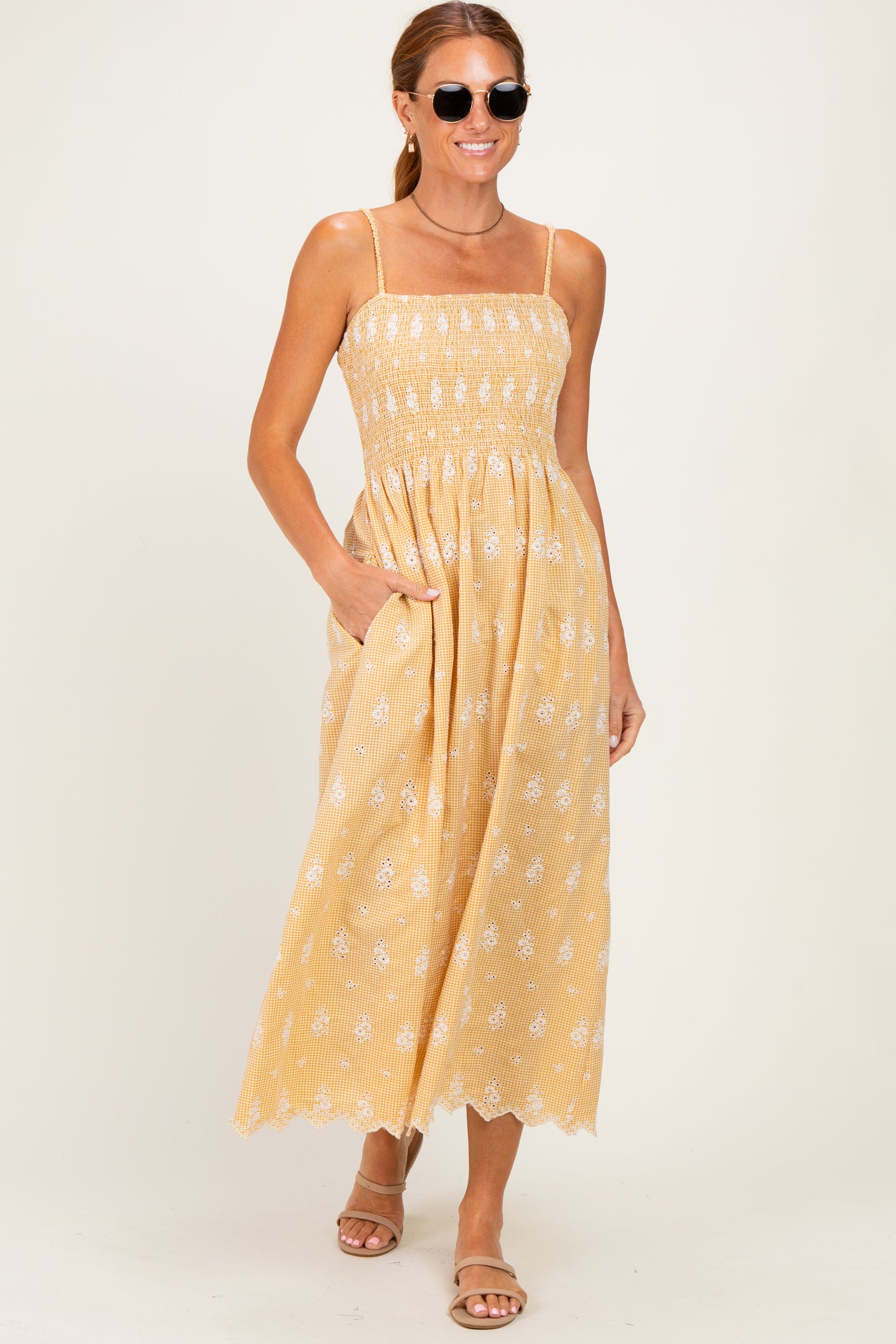 woman wearing a yellow smocked maxi dress with white floral patterns and pockets, paired with sunglasses and sandals