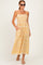 woman wearing a yellow smocked maxi dress with white floral patterns and pockets, paired with sunglasses and sandals