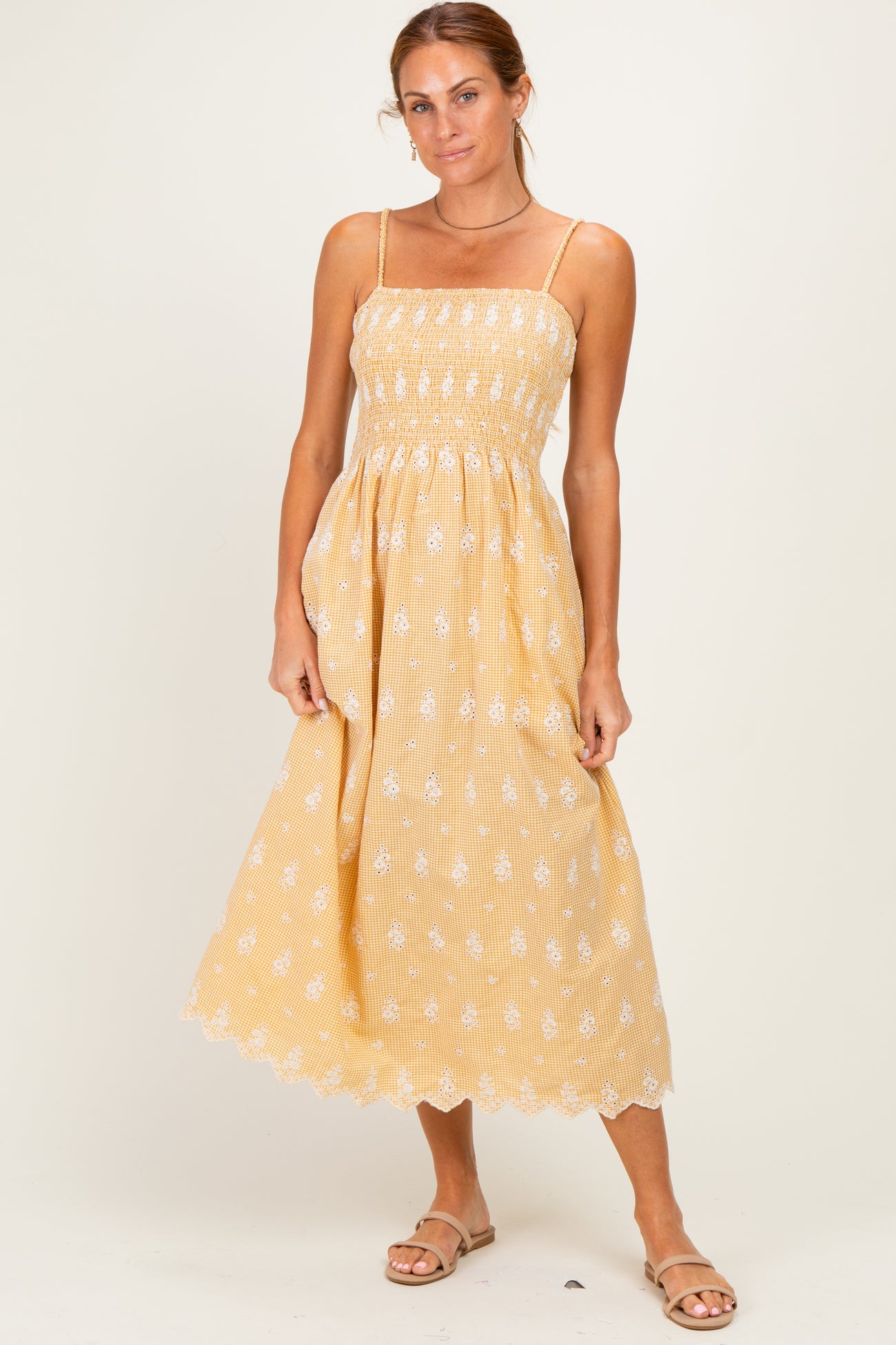 woman wearing a yellow midi sundress with white floral details and a smocked bodice, standing on a light background