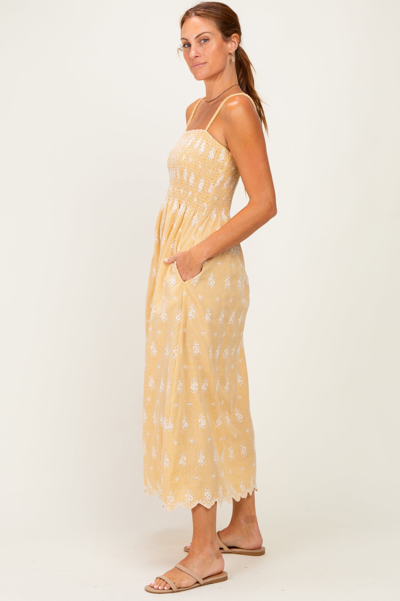 woman wearing a yellow embroidered maxi dress with a fitted bodice and pockets, styled with flat sandals