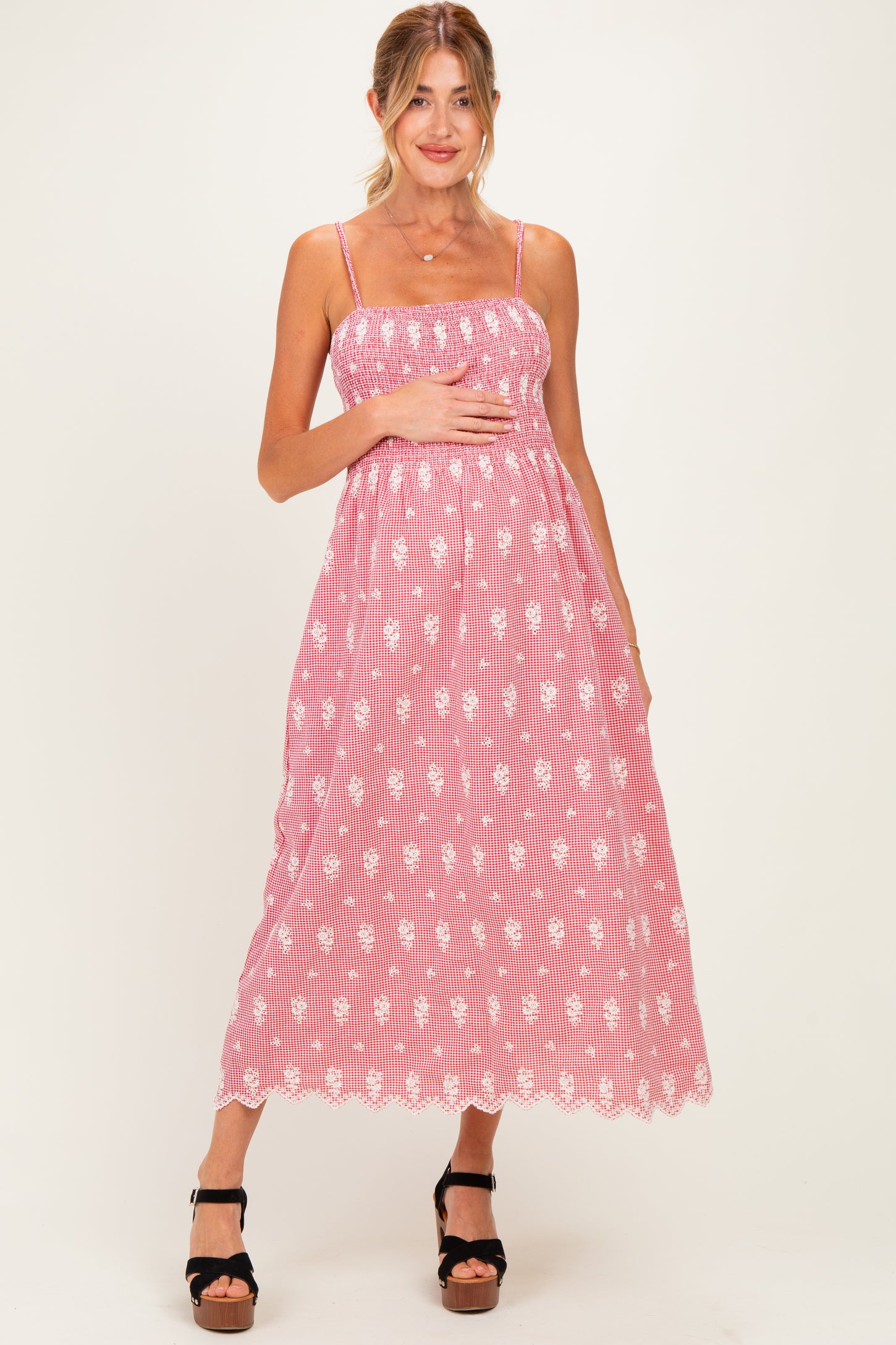 woman wearing a pink striped maternity dress with floral details and adjustable straps, holding her baby bump