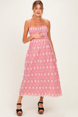 woman wearing a pink striped maternity dress with floral details and adjustable straps, holding her baby bump