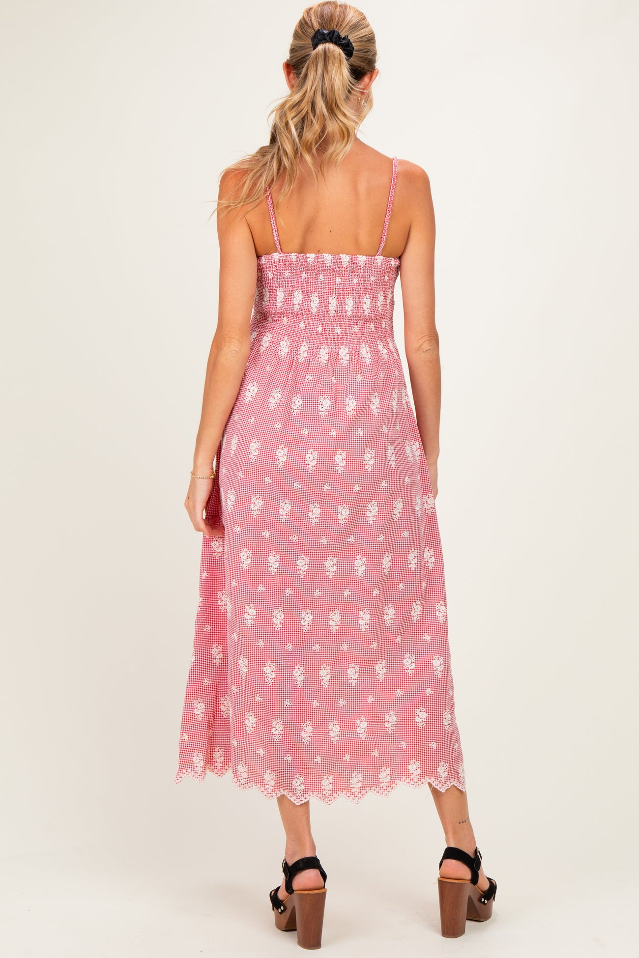 woman wearing a pink and white floral maternity midi dress with spaghetti straps and a smocked bodice, showing her baby bump