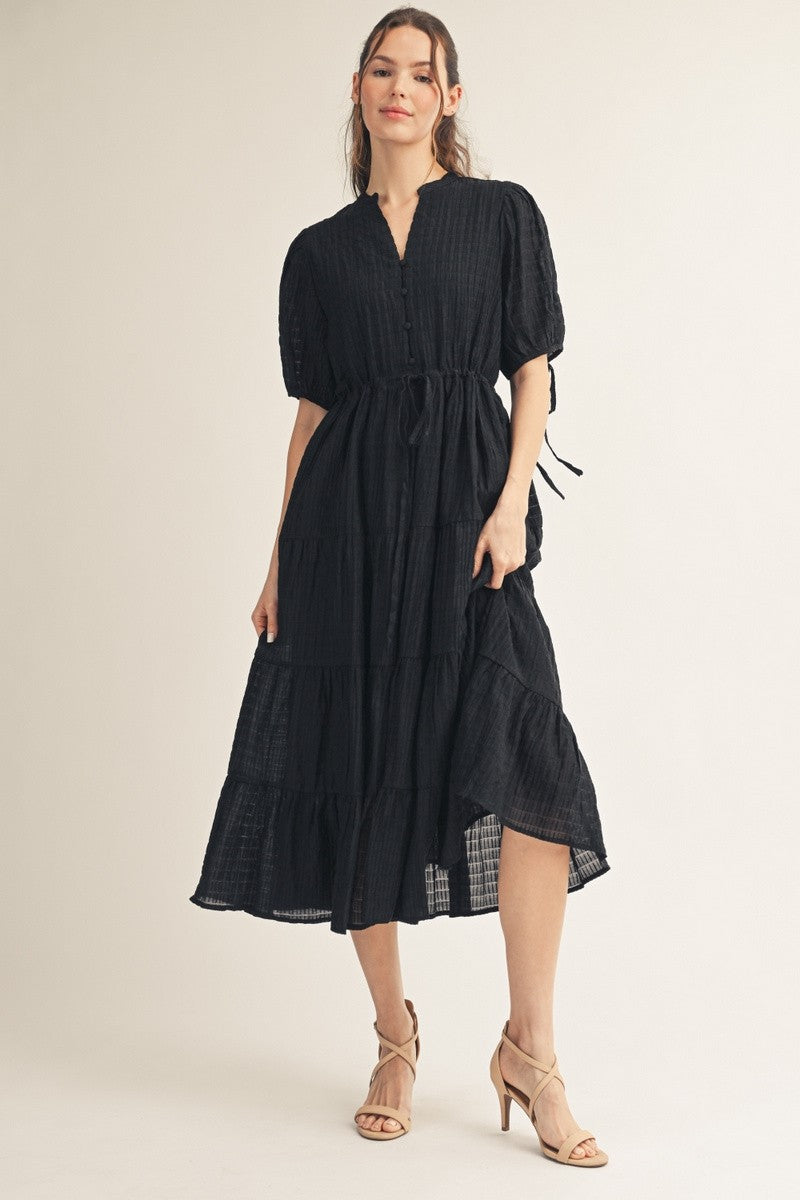woman wearing a black tiered midi dress with short sleeves and a tie waist detail