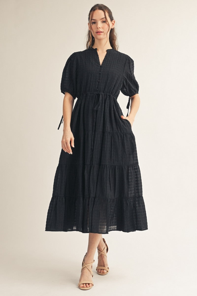 woman wearing a black tiered maxi dress with puff sleeves and a tie waist detail