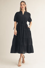 woman wearing a black tiered maxi dress with puff sleeves and a tie waist detail