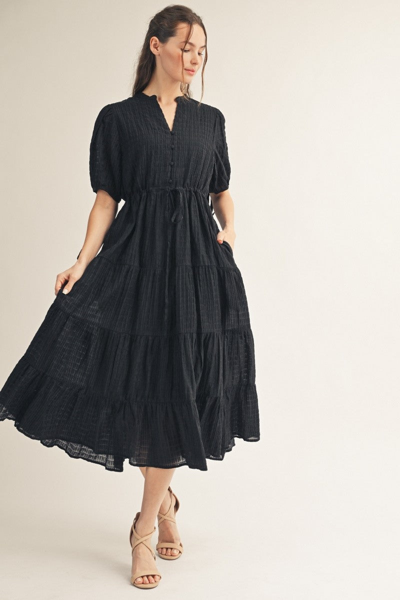 woman wearing a black tiered maxi dress with a button-down front and puff sleeves, standing gracefully