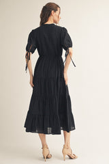 woman wearing a black tiered maxi dress with puff sleeves and a tie waist, shown from the back