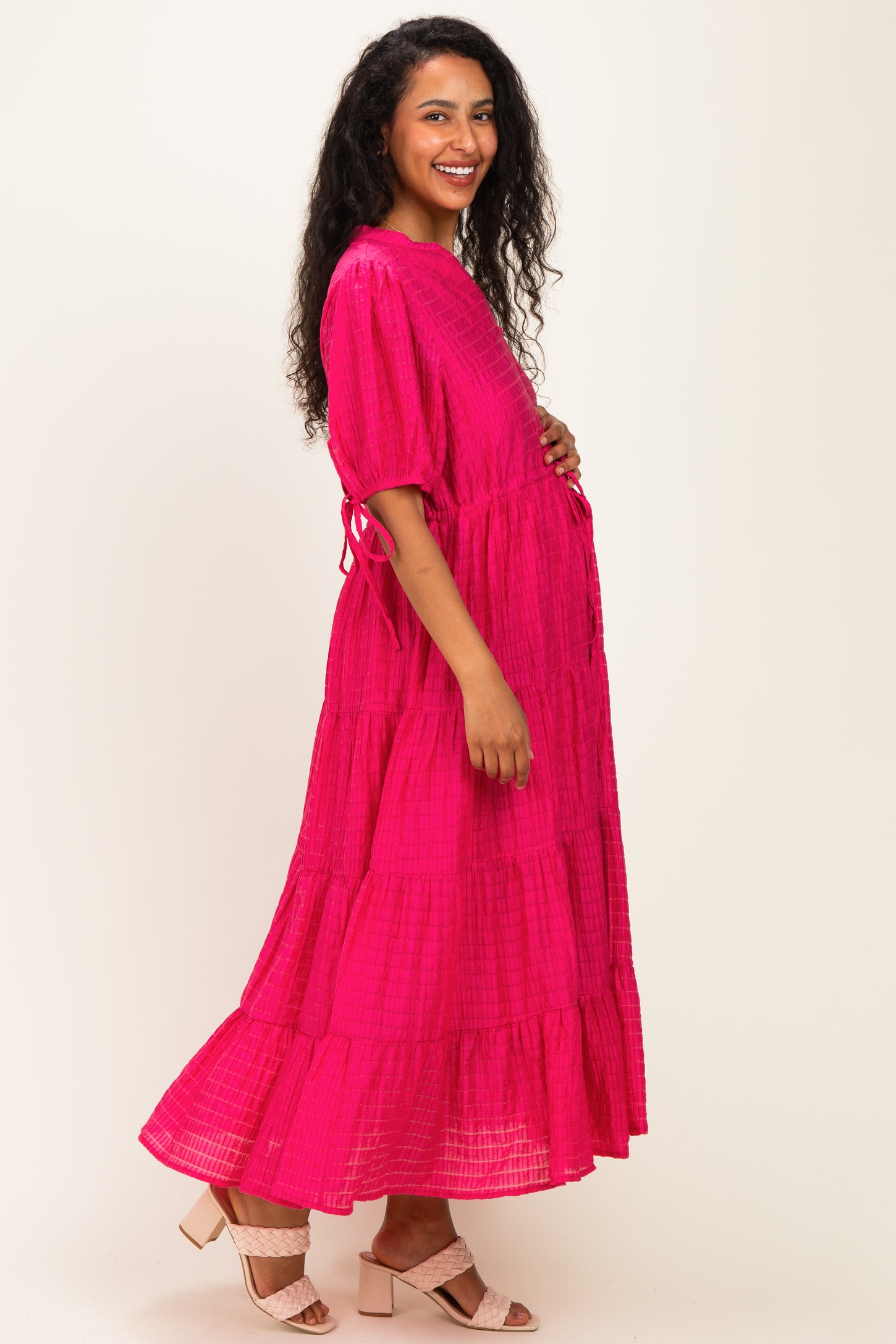 woman wearing a bright pink tiered maternity dress, smiling and showing a baby bump