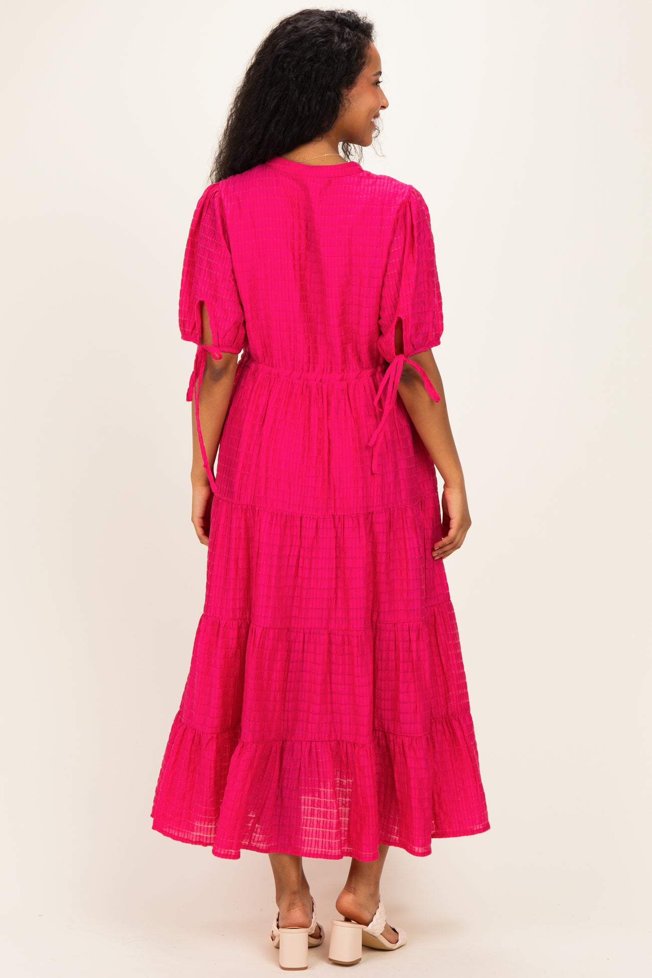 woman wearing a bright pink maternity maxi dress with tiered detailing and puff sleeves, showing a relaxed fit from the back