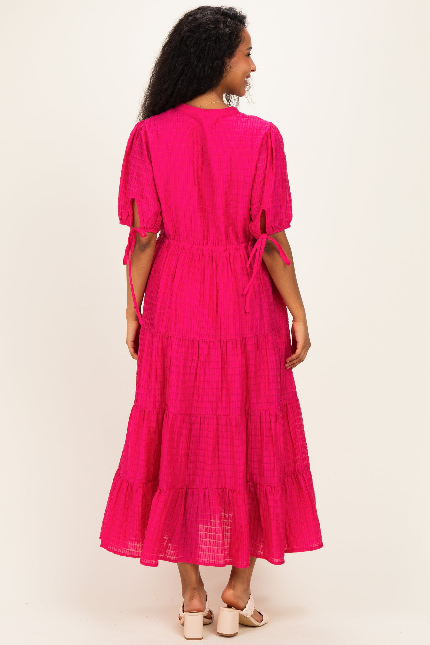 woman wearing a bright pink maternity maxi dress with tiered detailing and puff sleeves, showing a relaxed fit from the back