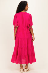 woman wearing a bright pink maternity maxi dress with tiered detailing and puff sleeves, showing a relaxed fit from the back