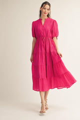 woman wearing a bright pink tiered maxi dress with short puff sleeves and a tie waist detail