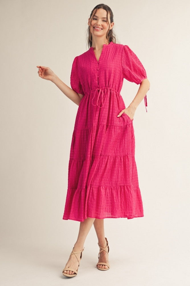 woman wearing a fuchsia tiered midi dress with short puff sleeves and a tie waist detail