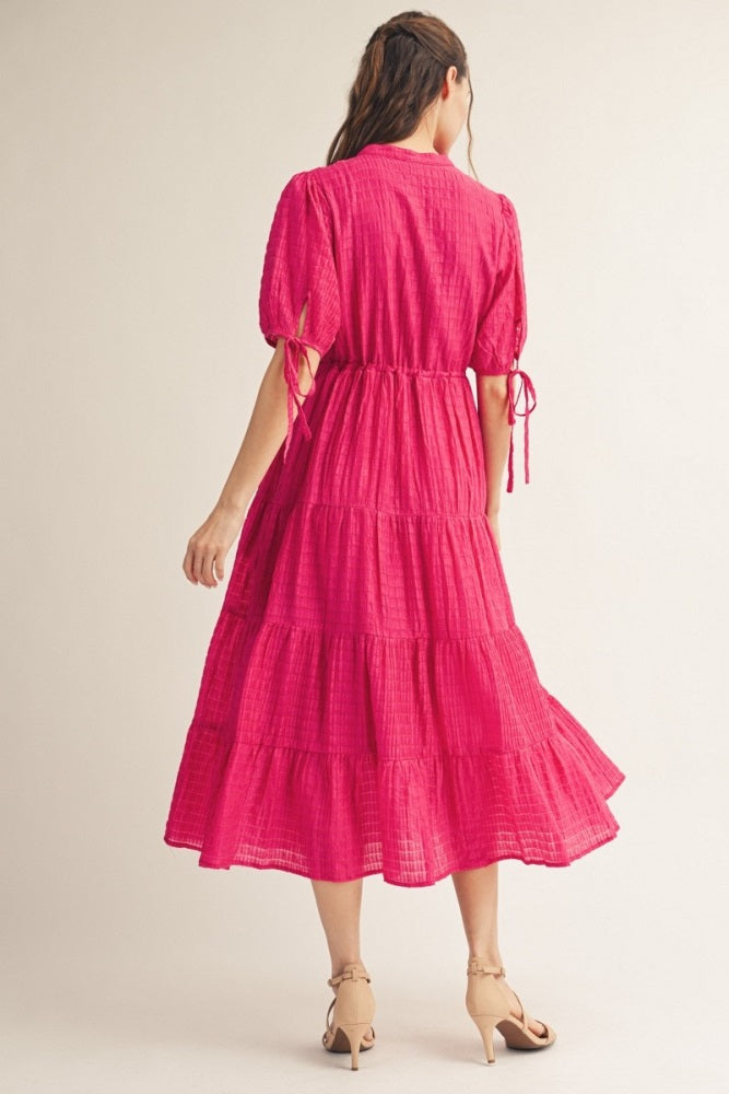 woman wearing a pink tiered midi dress with puff sleeves and tie details at the waist, seen from the back