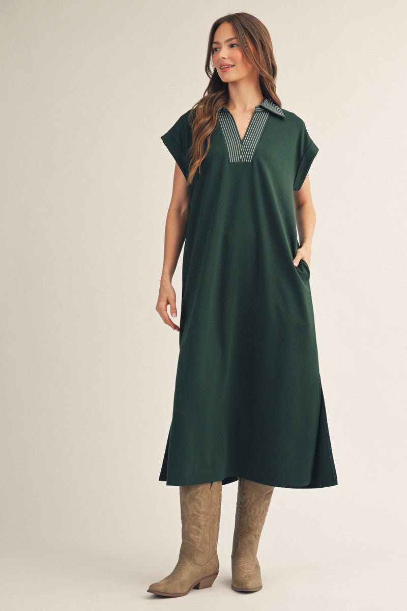 woman wearing a dark green oversized dress with a collared neckline and pockets, paired with beige cowboy boots