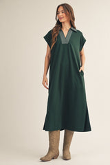 woman wearing a dark green oversized dress with a collared neckline and pockets, paired with beige cowboy boots