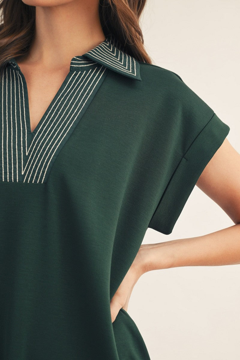 woman wearing a dark green short sleeve polo top with a v-neck and striped detailing on the collar