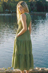 woman wearing a green tiered maxi dress with polka dots and pockets, standing by a lake